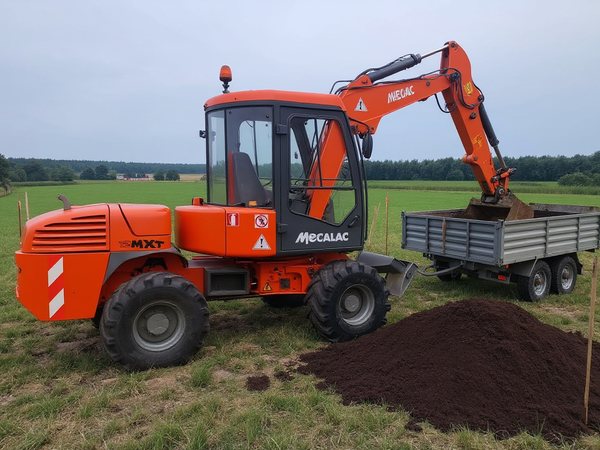 Mecalac 12 MXT ładuje ziemię na przyczepę na placu budowy
